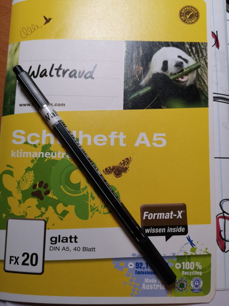 Das ist ein Schulheft, ein kleines Schulheft. Es hat keine Linien. Und man sieht einen schwarzen Stift. Der Stift ist von der Firma Stabilo. Auf dem Stift und auf dem Heft steht der Name Waltraud. Stift und Hefte waren ein Geschenk.