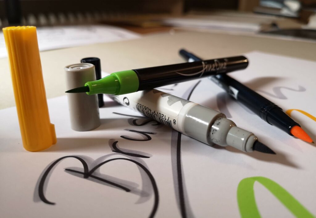 Auf dem Bild sieht man Brushpens oder Pinselstifte in Grün, Grau und Gelb. Diese Stifte sind zum Setzen von Akzenten ideal. Deshalb sollte das Papier sehr glatt sein, damit die Pinselstifte nicht ausfransen.