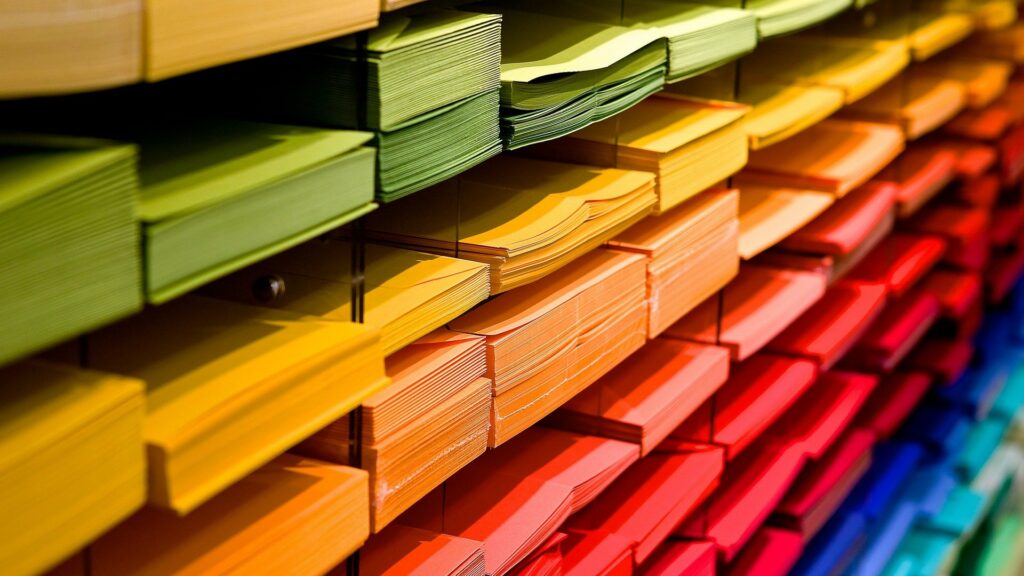 Auf dem Bild sieht man buntes Papier, das nach den Farben Grün, Gelb, Orange, Rot geordnet ist.