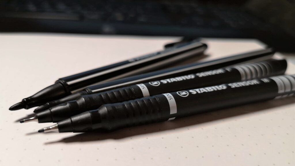 Auf dem Bild sieht man vier schwarze Stifte, die sehr gut zum Zeichnen und Sketchnoten geeignet sind. Sketchnotes mit diesen Stiften sehen immer gut aus.
